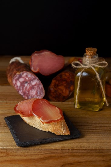 Tapa of iberian loin on rustic bread with olive oil on a black slate with black background