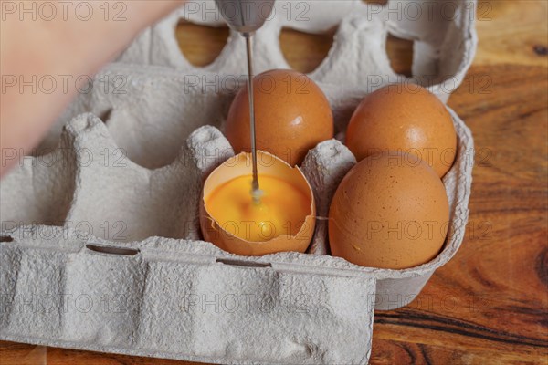 Woman beating an egg in its own shell with a small blender