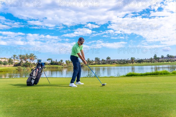 Male golf player on professional golf course. Golfer hitting the ball with driver stick next to a lake