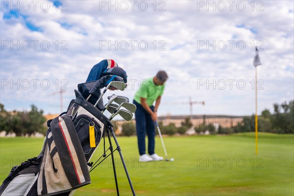 Caucasian professional golf player on the green preparing for the shot next to the fairway carrying bags