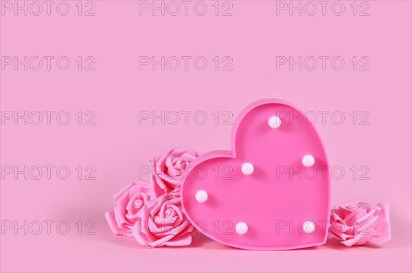 Valentine's day composition with roses and heart shaped lamp on pink background with copy space