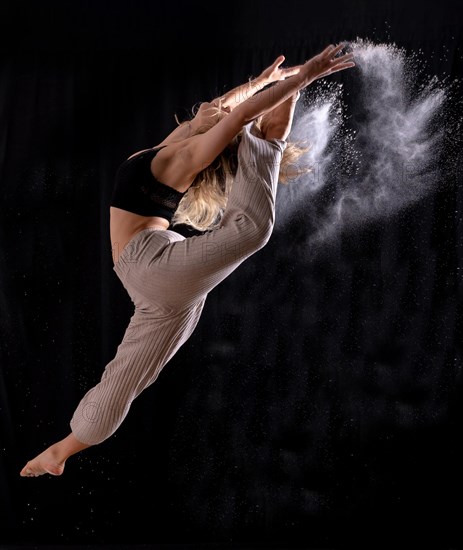 Young dancer performing a jump on a black background