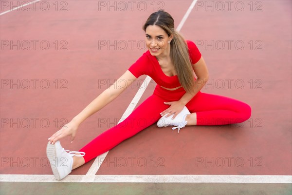 Fit woman in red outfit stretching in a city park