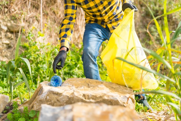 Unrecognizable man's hand picking up a plastic bottle in a forest. Ecology concept