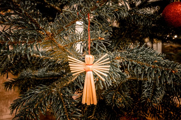 Christmas tree with an angel made of straw and a red Christmas tree ball