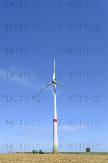 Wind turbine at a stubble field with round bales of straw