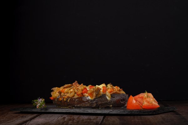 Eggplants stuffed with meat and vegetables with rosemary branch in flower and tomato cut on a black background