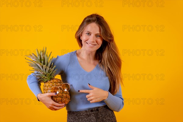 Woman with a pineapple in sunglasses in a studio on a yellow background