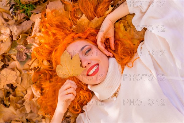 Red-haired woman lying on leaves in a park in a forest