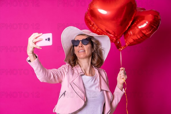 A blonde caucasian woman having fun with a white hat and sunglasses in a nightclub with some heart balloons