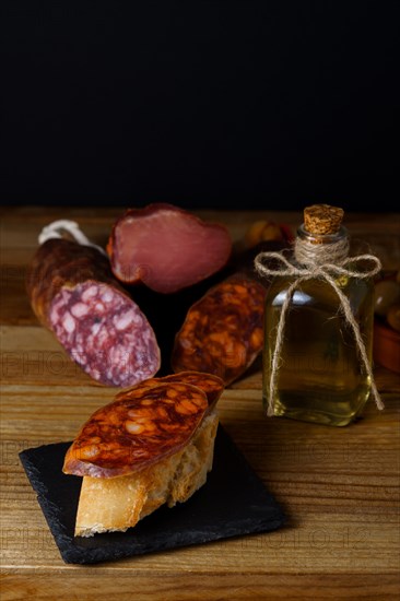 Tapa of iberian chorizo on rustic bread with olive oil on a black slate with black background