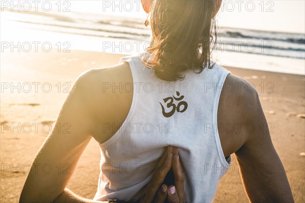 Rearview shot of a young woman practicing yoga at the beach