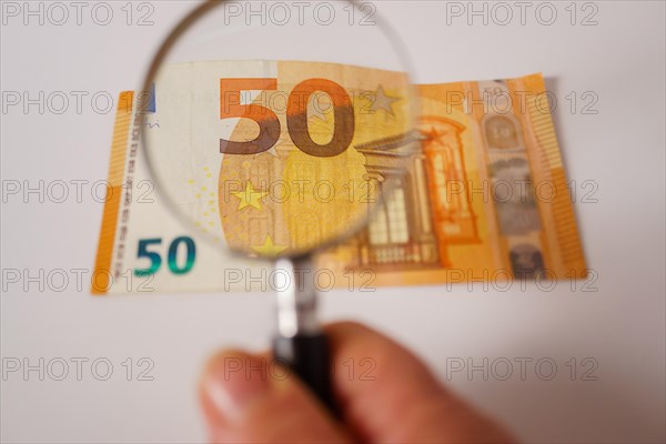 Fifty euro banknote seen with a magnifying glass on a white background and copy space