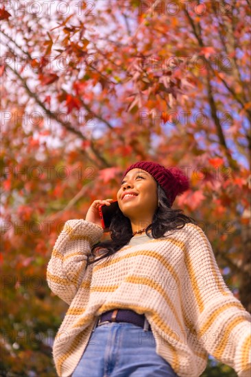 Asian girl in autumn with a mobile making a call in a forest of red leaves