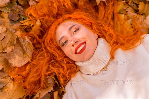 Red-haired girl lying on leaves in city park