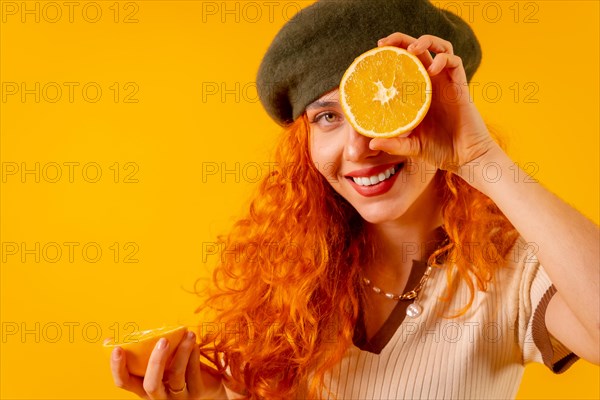 Redhead woman holding an orange over isolated yellow background