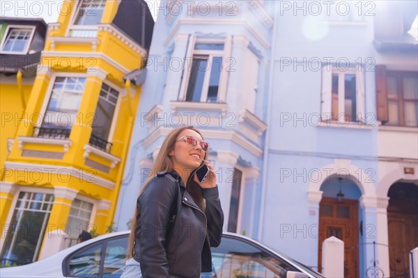Smiling young blonde woman in leather jacket talking on the phone