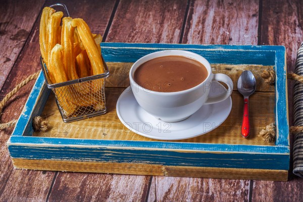 Hot chocolate in a white mug with churros in a blue wooden tray on a wooden table