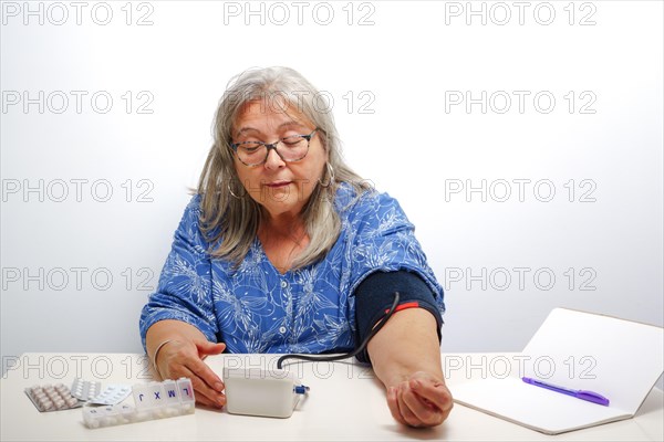 Older white-haired woman with glasses taking her blood pressure at home with white background