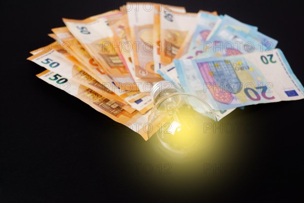 Lighted light bulb with euro banknotes in the background on a black background