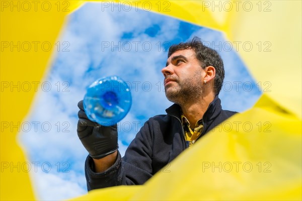 Man throwing a bottle into a garbage bag on the beach. Ecology