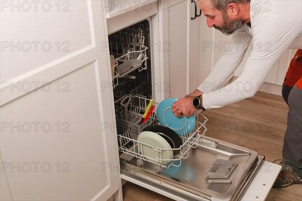 Man in white t-shirt putting the dishes in the dishwasher