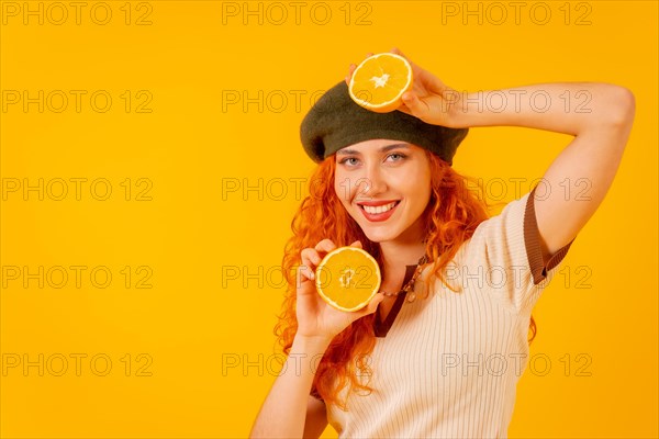 Teenager redhead girl holding an orange on isolated yellow background