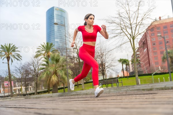 Athlete woman in red clothes running fast in the city