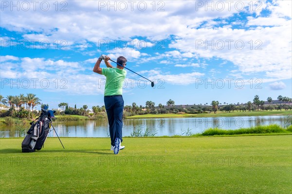 Man playing golf at golf club by a lake