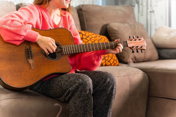 Playing the guitar at home sitting on the sofa in her living room next to the sale