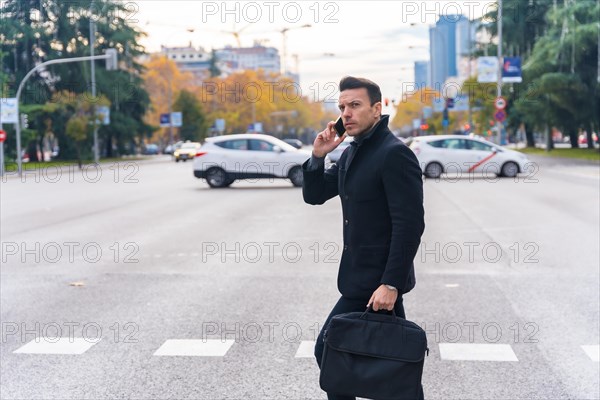 Middle-aged Caucasian businessman talking on the phone crossing the road in the city