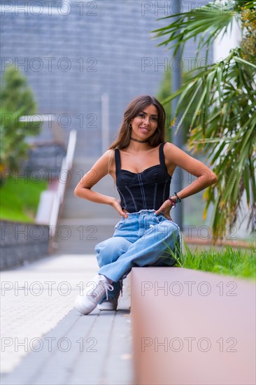 Portrait of a young brunette model in a black cap and jeans sitting in the city