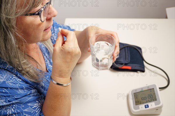 Older white-haired woman taking a pill after having her blood pressure checked