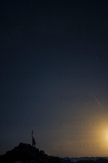 Mountaineer at summit cross of Namloser Wetterspitze at full moon and Lechtaler Alps