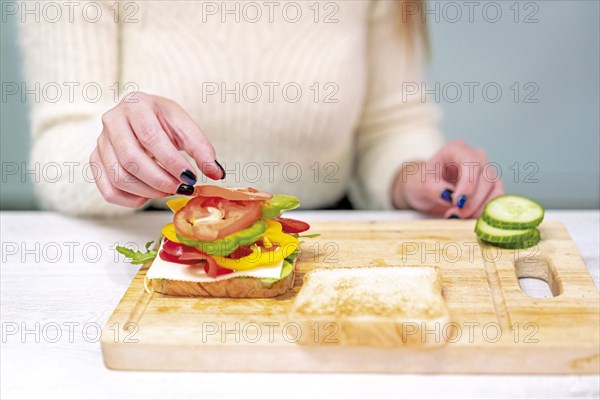 Unrecognizable person cooking a vegetable sandwich in the kitchen at home. Preparing it by putting tomato