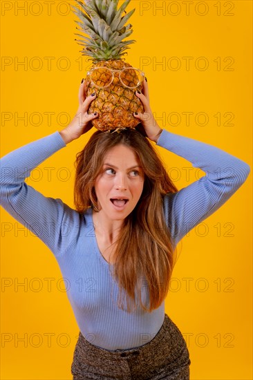 Portrait of a woman with a pineapple in sunglasses in a studio on a yellow background