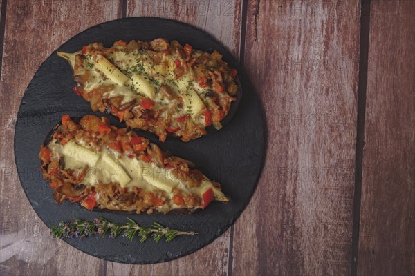 Foreground eggplant stuffed with meat and vegetables covered with bechamel sauce on a black slate on a wooden table