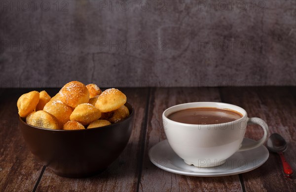 Homemade doughnuts with sugar in a bowl and hot chocolate in a white mug on a wooden table