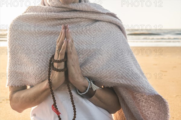 Close up of a woman clasping hands while holding a japa mala outdoors. Namaste pose