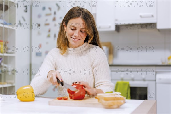 Vegetarian woman cooking a vegetable sandwich in the kitchen at home. cutting red pepper