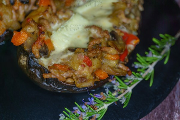 Foreground eggplant stuffed with meat and vegetables covered with bechamel sauce on a black slate on a wooden table
