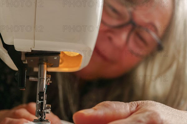 Older woman with white hair out of focus sewing a white fabric on a sewing machine