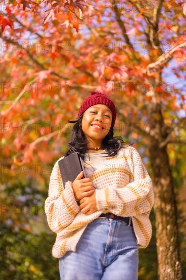 Portrait of asian girl in autumn with a tablet smiling in a forest of red leaves