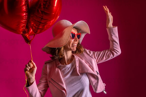 A caucasian woman with a white hat in a nightclub with some heart balloons