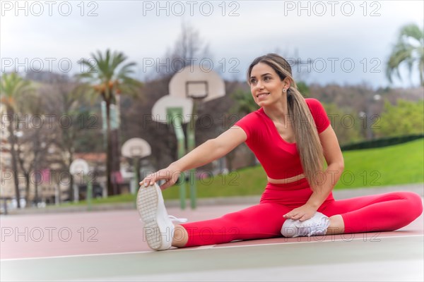 Fit woman in red outfit stretching in a city park