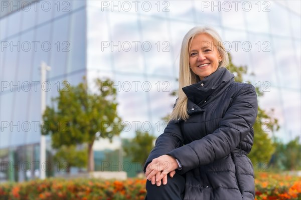 Corporate portrait of middle-aged businesswoman smiling near skyscraper exterior