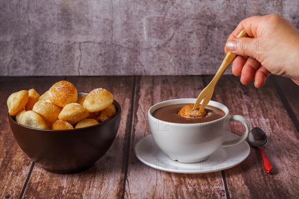 Woman spreading a sugared doughnut with a wooden fork on a hot chocolate in a white mug