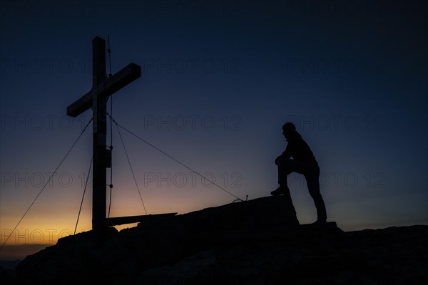 Mountaineers at the summit cross of the Namloser Wetterspitze at sunset with Lechtaler Alpen
