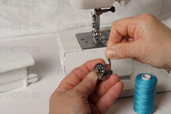 Close-up of a woman's hands putting blue thread on a sewing machine