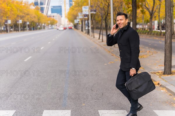 Middle-aged Caucasian businessman talking on the phone crossing the road on his way to work